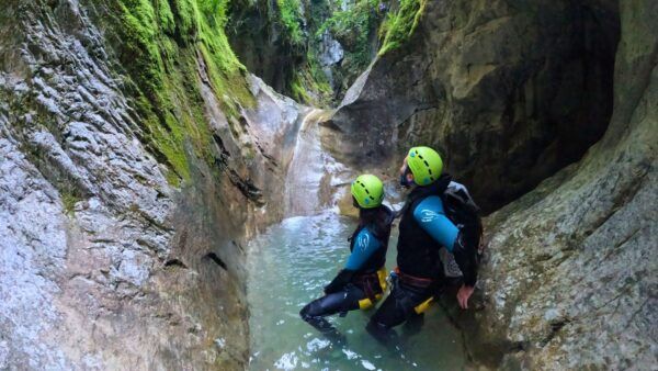 barranquismo-iniciacion-cerca-de-torla-ordesa Participantes en un barranco observando un tobogán natural rodeado de paredes de roca y vegetación en el Pirineo aragonés.